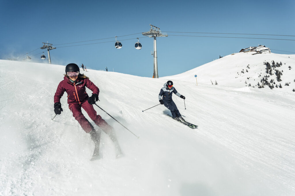 Paar beim Skifahren auf der Schmittenhöhe, dahinter die Gondelbahn