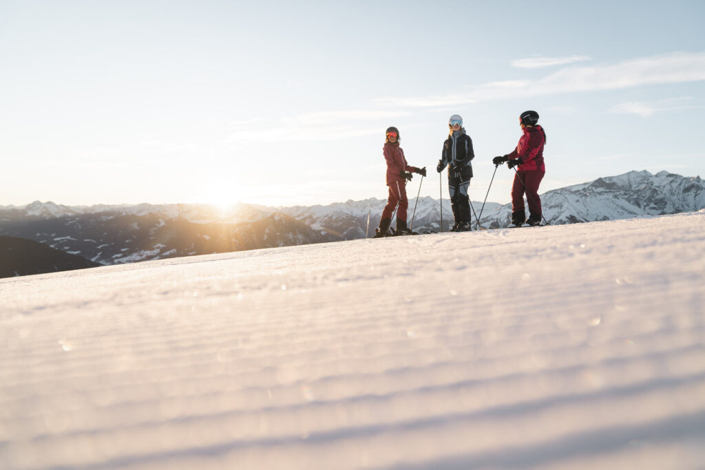 Three skiers with skis and poles on a freshly groomed slope in the morning